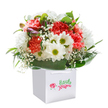 Like a breath of spring drifting through Harrow Weald, this bouquet delights the senses with its joyful palette and lush textures, arranged thoughtfully in a crisp white gift bag. Coral and peach carnations bloom exuberantly, their soft, ruffled petals gathered in the heart of the display, surrounded by luminous white daisies with lively yellow-green centers-each blossom seeming to sing with happiness. Wisps of baby's breath dot the bouquet with airy white clouds, adding a gentle delicacy, while on the left, hints of closed buds tinged with purple promise new beginnings. Polished dark green foliage embraces the base of the arrangement, layering in a deep, natural luster, much like the gardens in the heart of Harrow Weald. The white gift bag, set off with elegant ribbon handles, signals a ready-to-gift flair-ideal for celebrating a birthday, sending love, or offering comfort to someone dear. Photographed in the clean clarity of professional studio light, every colour and curve is alive, making this bouquet a radiant expression of the hope and warmth nurtured by Harrow Weald's most dedicated florists.